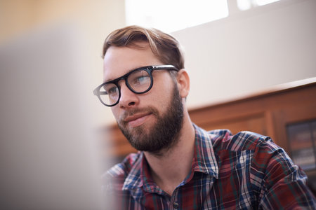 Using all the latest tech. a handsome young hipster working on a laptop.の写真素材