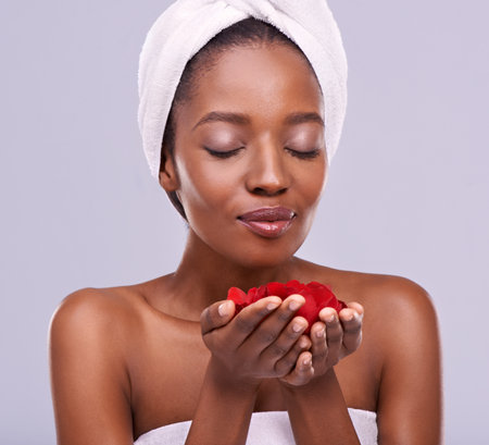A rose and her petals. A studio shot of a beautiful young woman holding red petals and wearing a towel on her head.の写真素材