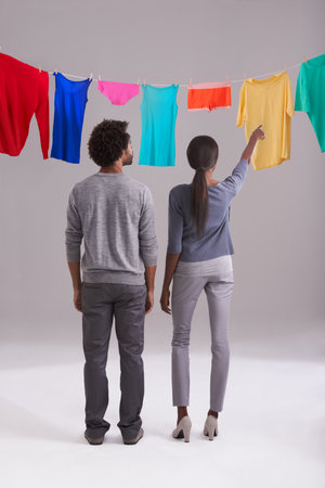 And thats how you hang up the washing. Studio shot of a young couple standing in front of a washing line full of colorful laundry.の写真素材