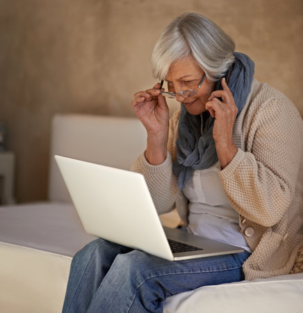 Im checking my emails now...A senior woman on her mobile while using her laptop at home.の写真素材