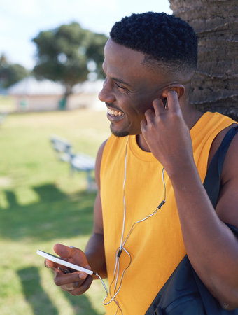 African american man using smartphone listening to music relaxing outdoors in park enjoying summer
