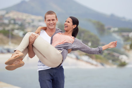 Ill carry her to the ends of the earth. a handsome young man carrying his girlfriend on the beach.