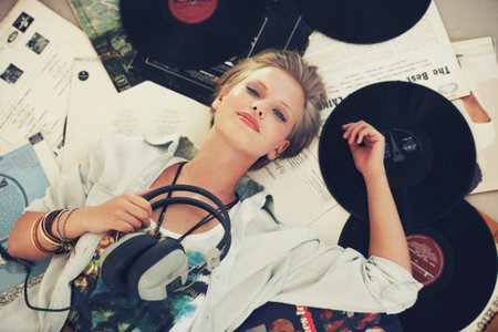 Hay Mr DJ put the record on. A beautiful young woman listening to music while lying on her back surrounded by records.の写真素材