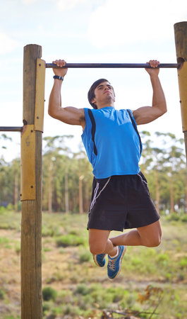 Determination is everything. Young adult male using outdoor gym apparatus.