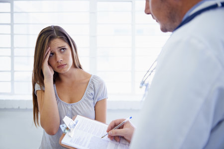 So, how long have you been having these headaches. A young woman looking concerned during a visit to the doctor.の写真素材