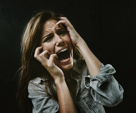 The face of desperation. A young woman screaming uncontrollably while isolated on a black...
