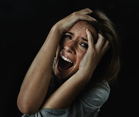 Please...help me. A young woman screaming uncontrollably while isolated on a black background.の写真素材