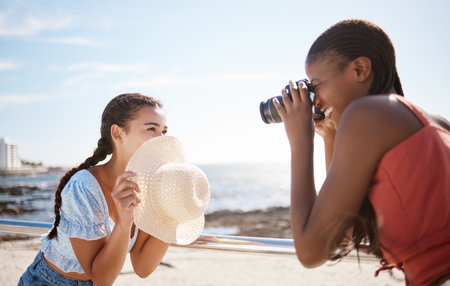 Photographer, woman and model at the beach in summer shooting a creative, freedom and happy outdoor pictures. Photography, smile and fun girl holding a camera with focus on female and ocean backdropの写真素材