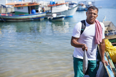 Fishing is my life. Portrait of a fisherman standing with a fish next to his boat.の写真素材