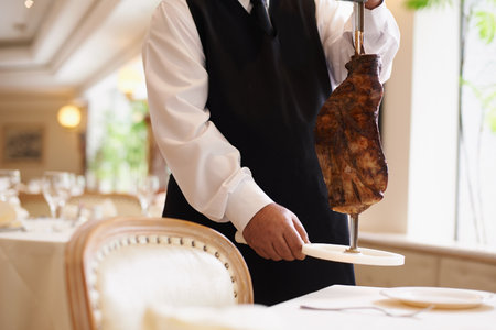 That looks delicious. Cropped image of a male waiter holding a skewer with a large piece of meat on it.の写真素材