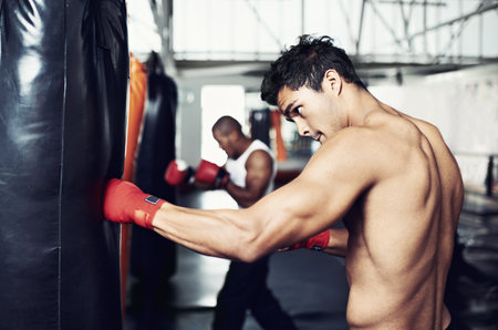 Hes dedicated to the sport of boxing. a young male boxers training on heavy bags.の写真素材