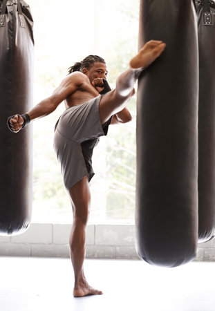 Aiming for the head. a young kick boxer practicing on a punching bag in a gym.の写真素材