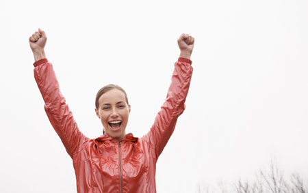 Taking her run one step at a time. a young woman standing with her arms raised in victory while out...