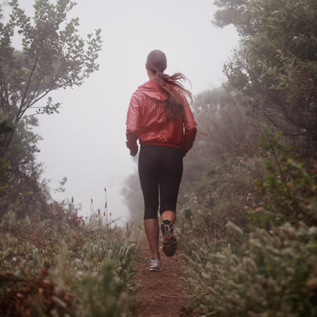 She found the path to longevity. Rearview shot of a woman running on a trail on a misty morning.の写真素材