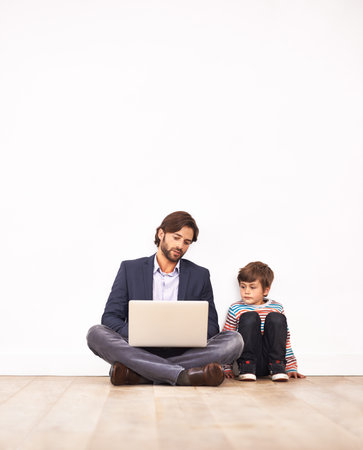 Modern parenting. A father and his young son sitting on the floor and looking at a laptop together.の写真素材