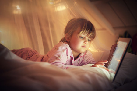 I read past my bedtime. A young girl lying on her bed while using a digital tablet.の写真素材