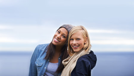 Friendship and laughter can warm up any day. Two happy young women smiling on the beach.の写真素材