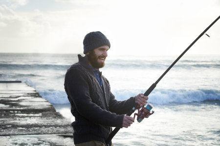 Taking his time for the big catch. a solo fisherman fishing off a pier at the ocean.の写真素材