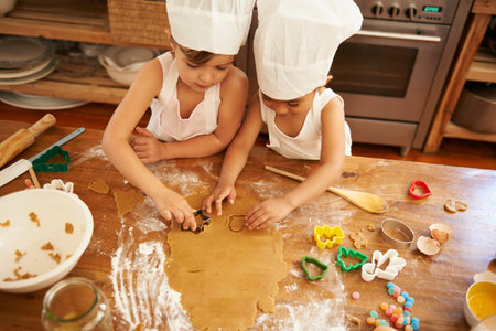 Baking is so much fun. High angle view of two little girls baking cookies in the kitchen.の写真素材