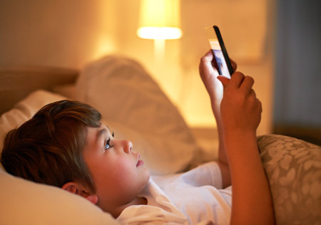 From teddybears to tablets. a young boy using a digital tablet while lying in bed.の写真素材