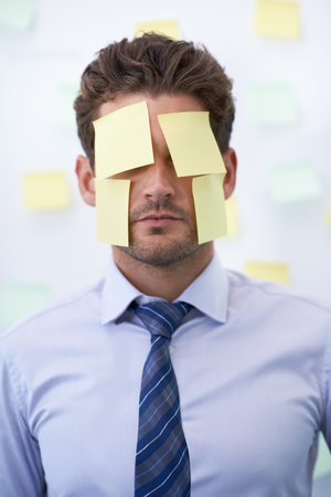 Hiding from his responsibilities. a young businessman with a sticky notes covering his face.の写真素材