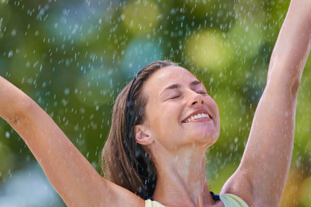 A young woman standing with her arms outstretched in the rain.の写真素材