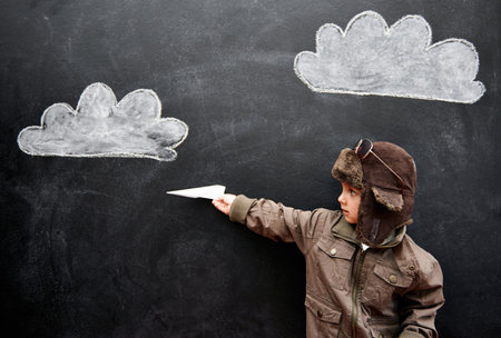 Ladies and gentlemen, this is your captain speaking...a little boy playing with an airplane in front of clouds drawn on a blackboard.の写真素材