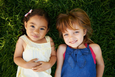 Too cute. High angle portrait of two little girls lying on the grass.の写真素材