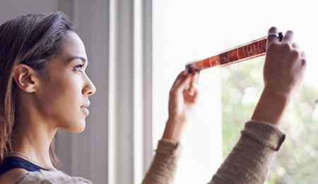A young woman looking at photographic negatives near a window.