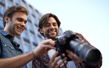 Hes proud of his photographs. Low angle shot of two men looking at the lcd screen on a digital camera.の写真素材