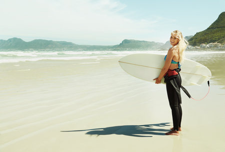 On her way into the ocean. A young female surfer holding her surfboard while standing on a beach.