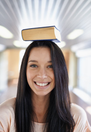 Shes excited to learn. Portrait of an attractive young student balancing a book on her head.の写真素材