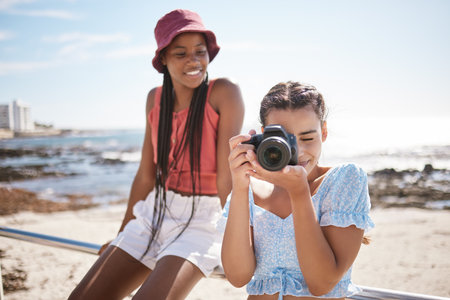 Summer, beach and photographer with camera, young girl taking a photograph. Friends, fun and happy teenagers on holiday by the sea with a scenic ocean view. Portrait of girls, photography and natureの写真素材