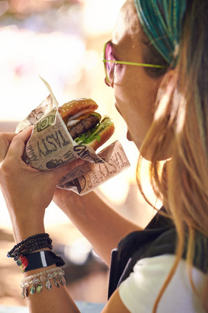 Fun in a bun. a young woman eating a hamburger outside.