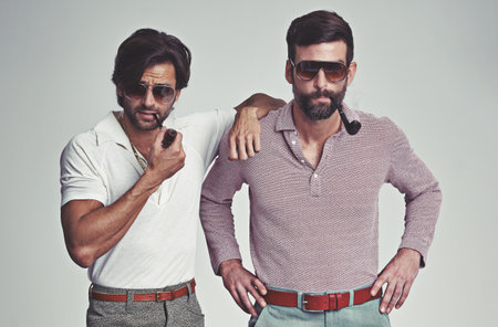 Theyve got far out style. Studio shot of two men standing together while wearing retro 70s wear and smoking pipes.の写真素材
