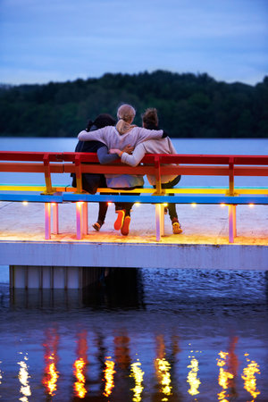 Moments of romance. Rearview shot of three women sitting on a bench on a pier over a lake.の写真素材