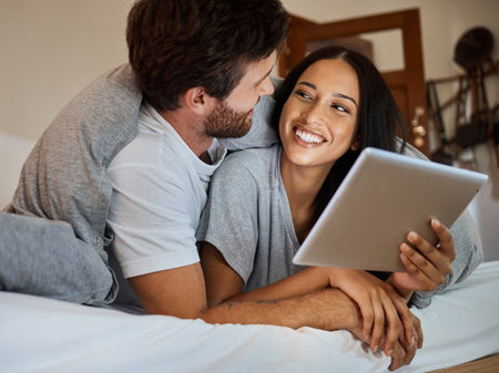 Happy couple, smile and tablet in bedroom entertainment, love and care relaxing together at home. Man and woman smiling for fun bonding time streaming on wifi in bed with touchscreen technologyの写真素材