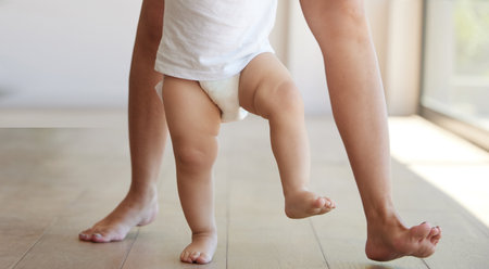 Baby, learning and walking with a child taking its first steps with his mother to learn to walk at home. Feet, legs and balance with a kid stepping forward for growth and development in the houseの写真素材