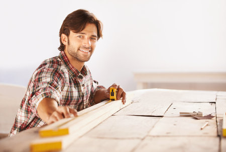 Hes skilled at his trade. A handsome young carpenter taking measurements of some wood.の写真素材