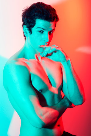 The face of confidence. A bare chested caucasian male looking at the camera covered by the tinge of a red and blue light.の写真素材