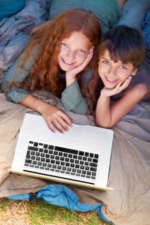 Accessing the web from the wilderness. A young brother and sister surfing the web while out camping.