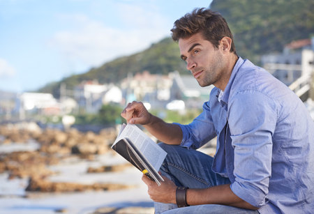 Novels are a great way to relax. A young man reading a book outdoors.の写真素材