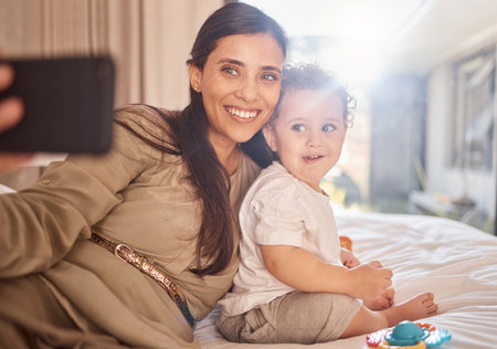 Smile, selfie and phone with mother and baby relax in bedroom for happy, digital and social media. Family, internet and love with mom and child for memory, lifestyle and wellness at home togetherの写真素材