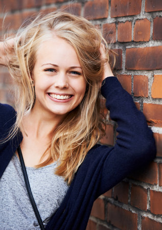 Confident and beautiful. Portrait of an attractive young woman leaning against a brick wall.の写真素材