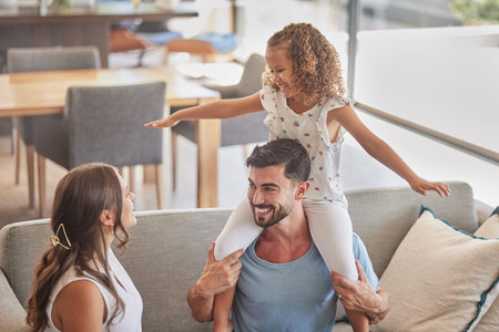 Children, family and love with a girl, mother and father playing on a sofa in the living room of their home together. Kids, happy and smile with a man, woman and daughter having fun in their houseの写真素材