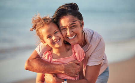 Portrait of grandmother and child at the beach on holiday, smiling and having fun. Senior woman with grandchild, hugging her by the ocean during sunset. Summer, vacation and family holiday at the seaの写真素材