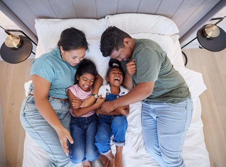 Family bed, home relax and parents in bedroom with children, care for comic kids and love in house together from above. Top view of girl siblings laughing with happy mother and father in the morningの写真素材