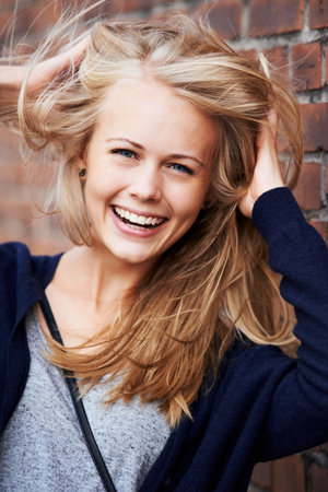 Confident and beautiful. Portrait of an attractive young woman leaning against a brick wall.の写真素材