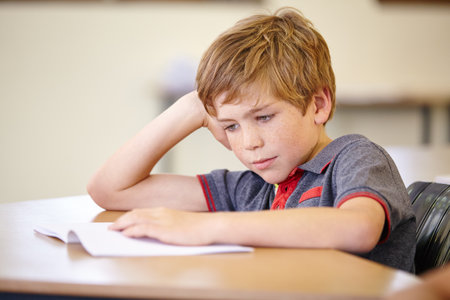 Classroom contemplations. A young student focused on his work while sitting at his school desk.の写真素材