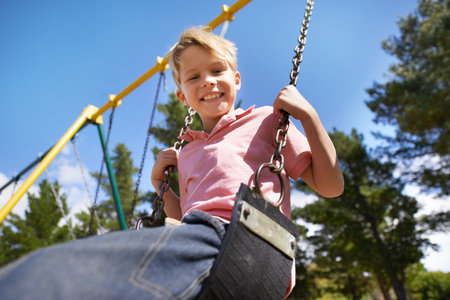 Higher and higher. A young boy enjoying the swings on the playground with friend.の写真素材
